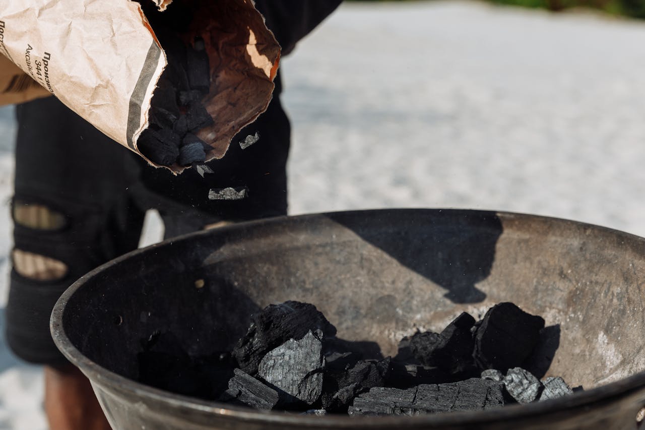 Detailed image of charcoal poured from a bag into a grilling basin outdoors.